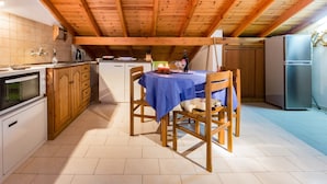 A kitchen with wooden cabinets, a dining table with chairs, a refrigerator, and a tiled floor. - Villa Perris Studios (Corfu)