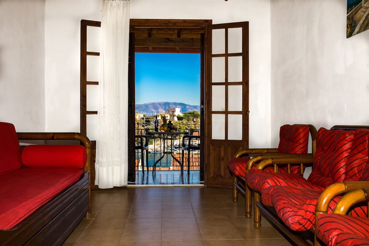 A room with a wooden bed, a sofa, and a view of a pool and mountains.