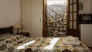 A bedroom with a bed, a nightstand, a lamp, a television, and a view of a stone staircase leading outside. - Villa Perris Studios (Corfu)