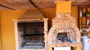 A brick-built outdoor oven with a chimney, a metal pot, and a wooden shelf.