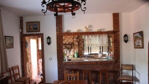 A dining area with a brick fireplace, wooden chairs, and a table with a basket of greens.
