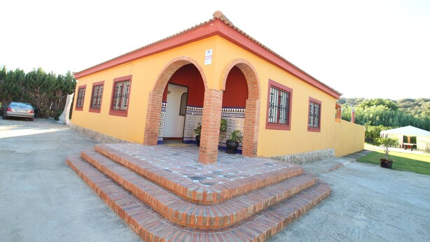 A yellow building with a red roof, featuring a central entrance with two arches and a tiled entrance area.