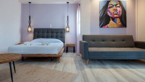 A modern bedroom with a bed, a sofa, a small table, and a painting on the wall. - Iliovasilema (Lemnos)