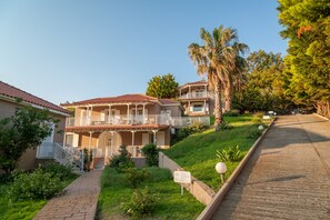 A two-story building with a balcony, surrounded by greenery and a paved pathway.