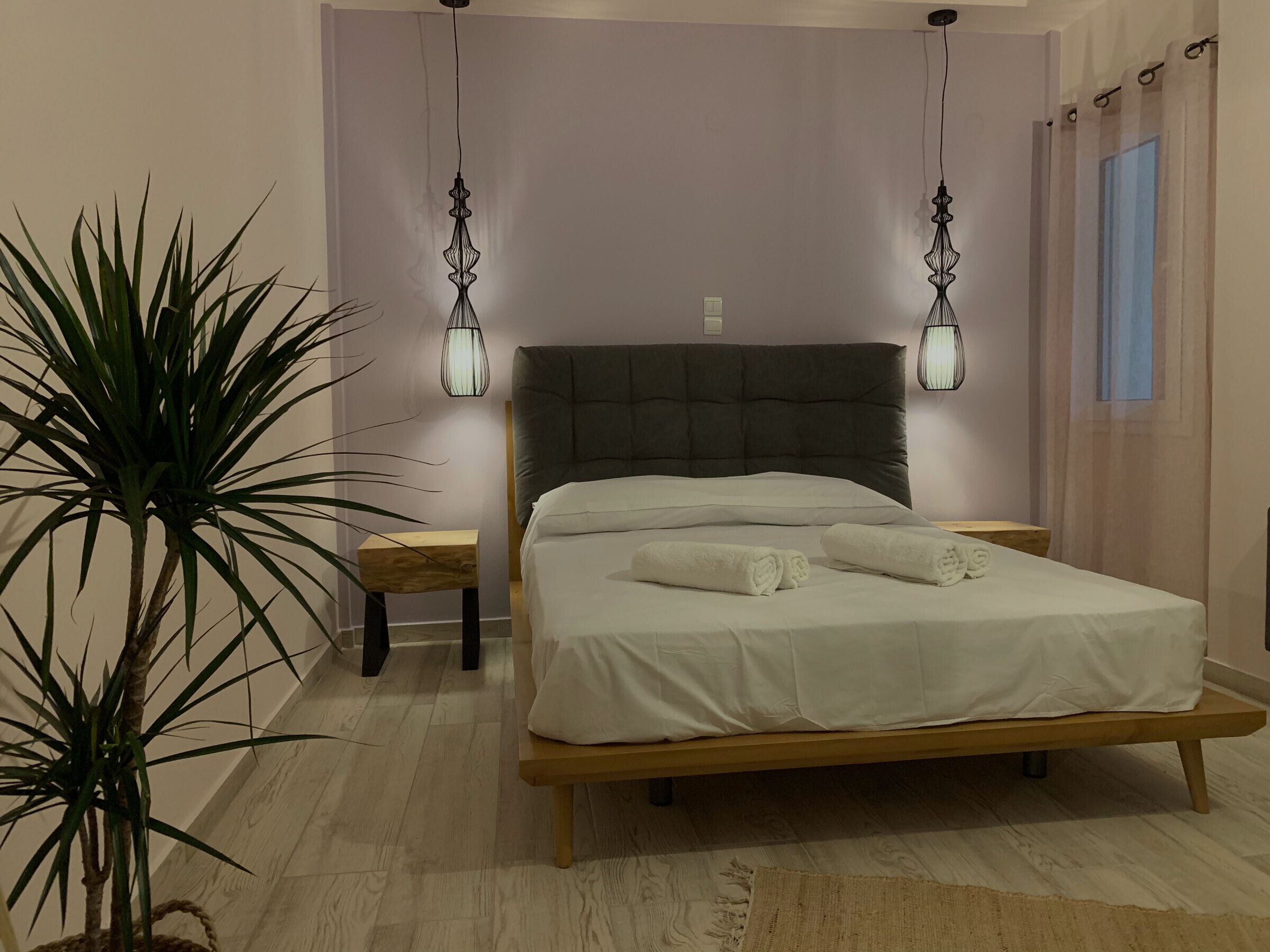 A bedroom with a bed, bedside tables, a potted plant, and hanging lamps.
