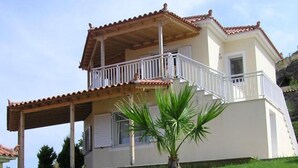 A two-story house with a balcony, a small garden, and a palm tree. - Iliovasilema (Lemnos)