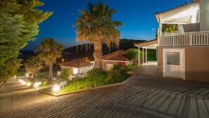 A residential area with houses, a palm tree, and a well-lit street at dusk. - Iliovasilema (Lemnos)