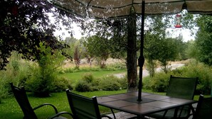 Une terrasse extérieure avec une table et des chaises, entourée de verdure et offrant une vue sur une rivière.