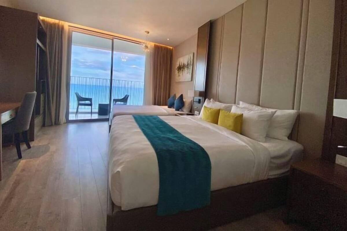 A hotel room with a large bed, a desk, and a balcony with a view of the sea.