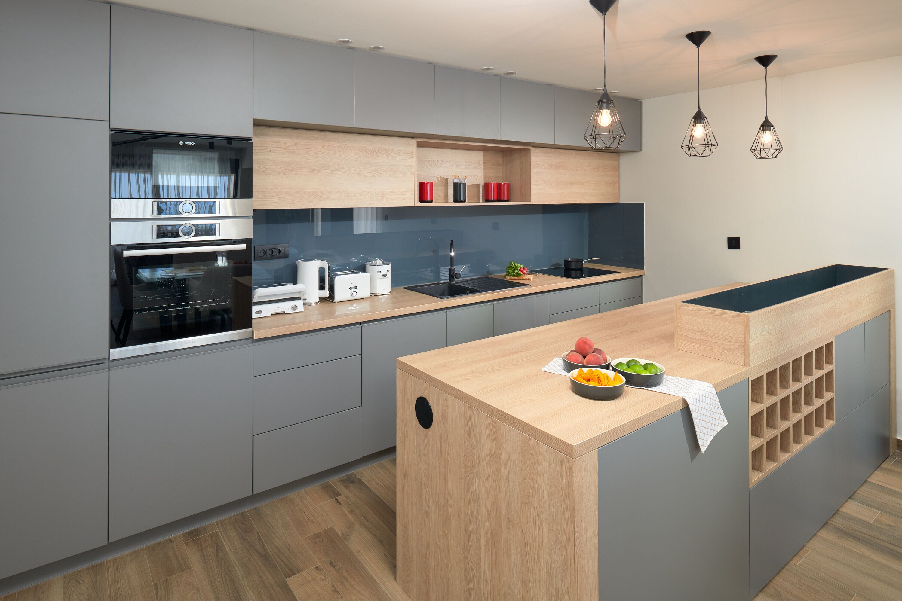 Eine moderne Küche mit grauen Schränken, einer Holztischinsel und einem eingebauten Backofen.