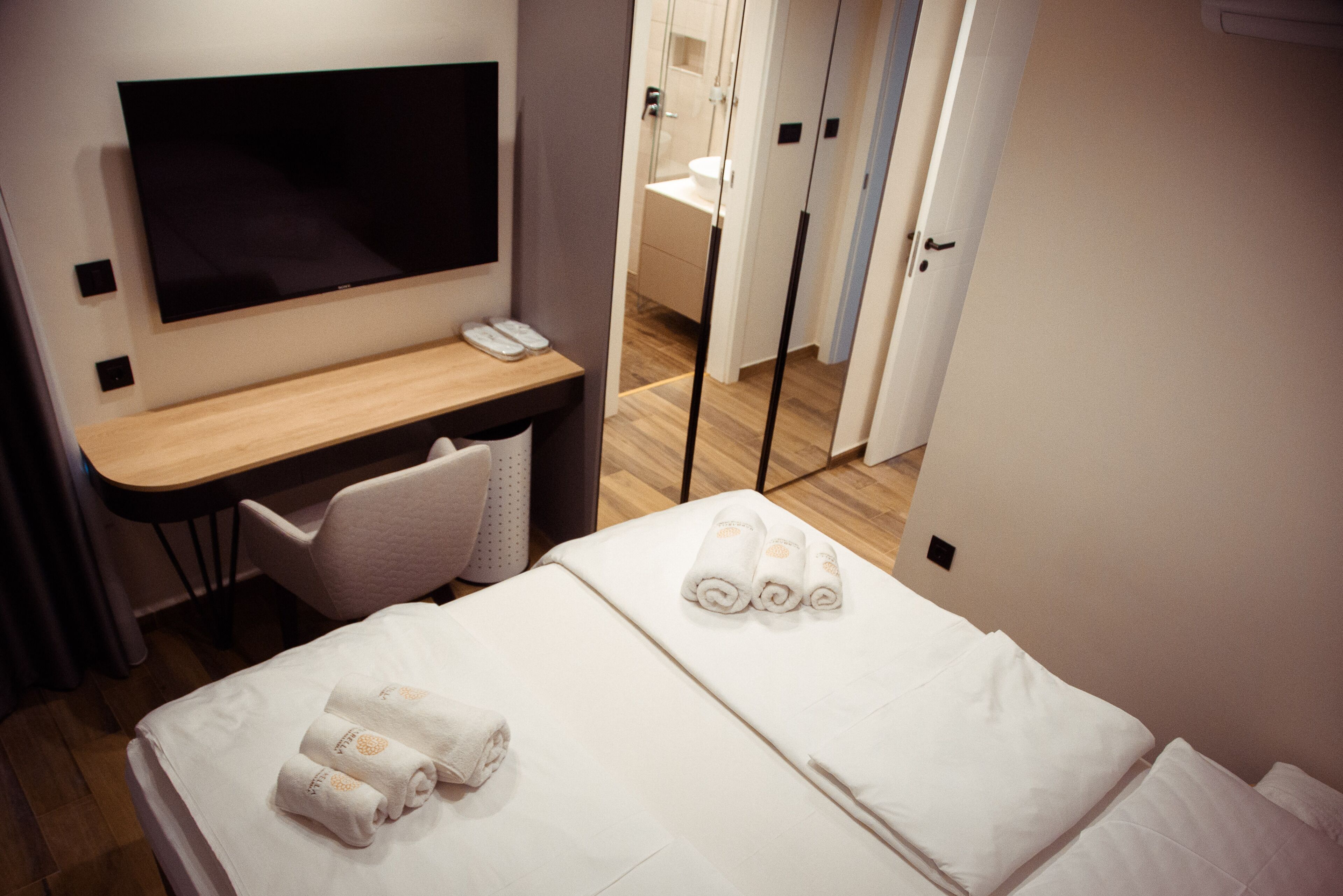 A hotel room with a bed, a desk with a chair, a television, and a bathroom visible through a door.