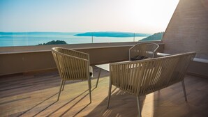 Een balkon met twee rieten stoelen en een kleine tafel, met uitzicht op een waterpartij en het landschap in de verte.