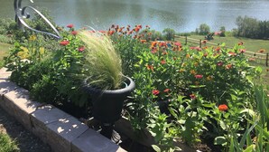 A lakeside garden with a metal sculpture, flowering plants, and boats on the water. - Water Views from most rooms-on the Rappahannock River (Locust Hill)