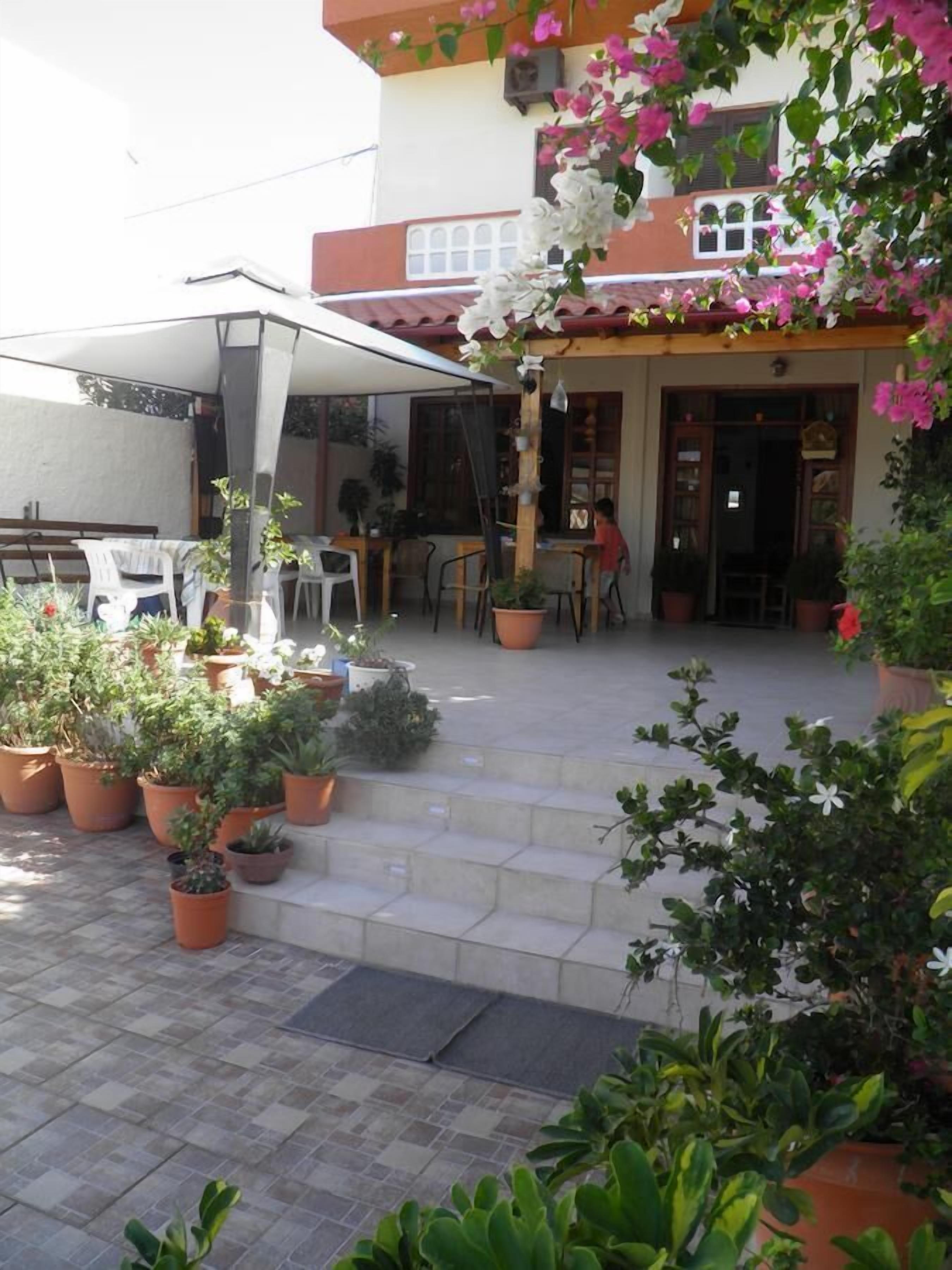 Eine Außenpatio-Terrasse mit Kübelpflanzen, einem überdachten Sitzbereich und einem Gebäudeeingang.