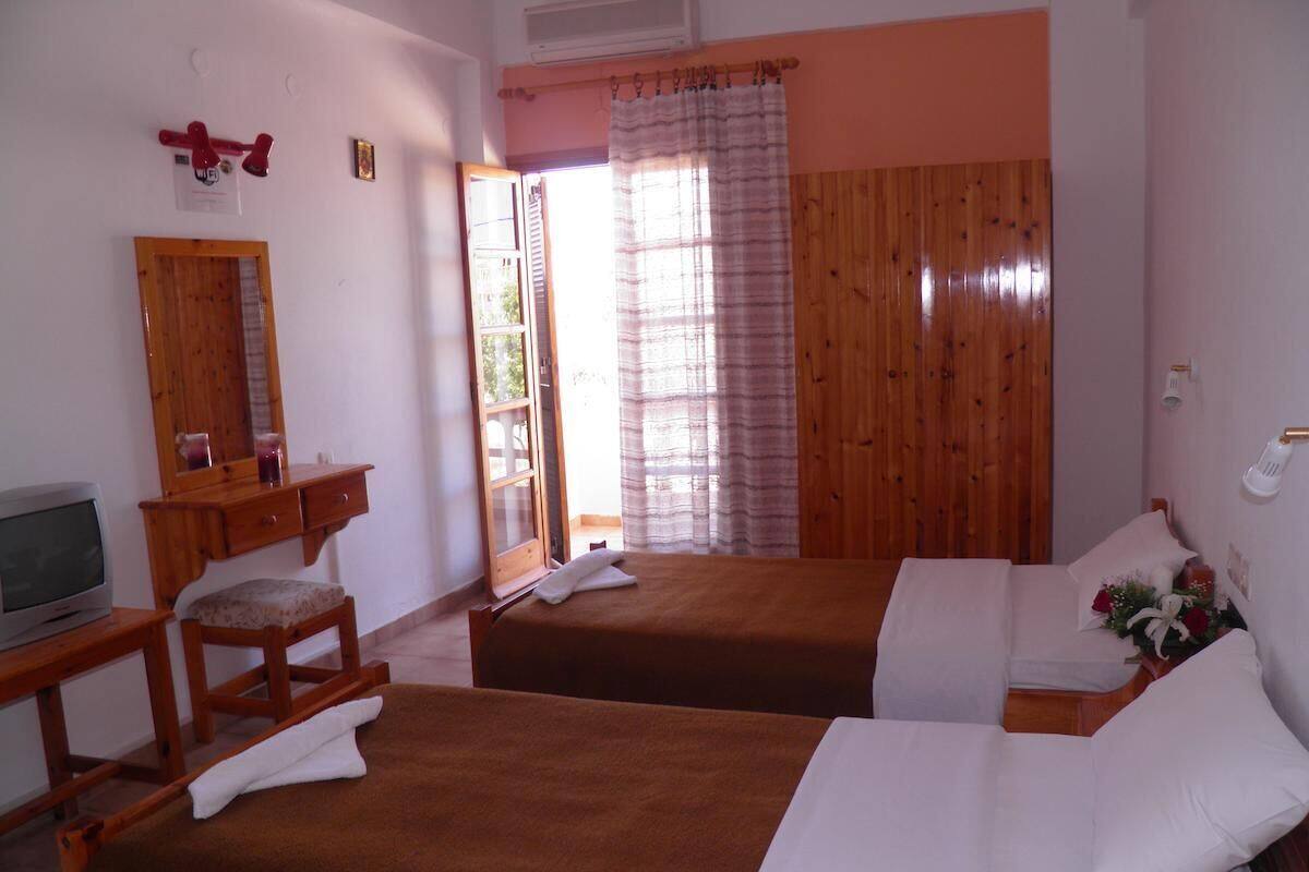 Una habitación con dos camas, un escritorio de madera, televisión, un espejo y una ventana con cortinas.