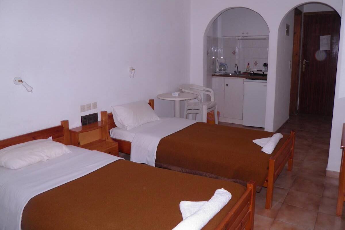 Habitación de hotel con dos camas, un pequeño rincón americano, una mesa redonda y una puerta que da a otra habitación.