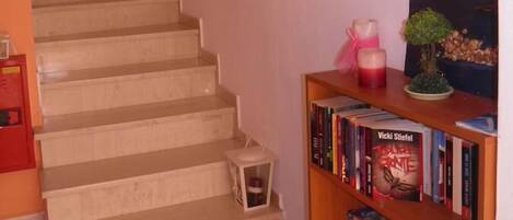 A staircase with a wooden handrail, a small white lantern, and a bookshelf with books and a small plant.
