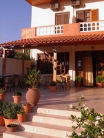 A two-story building with a tiled roof, outdoor seating area with tables and chairs, and potted plants.