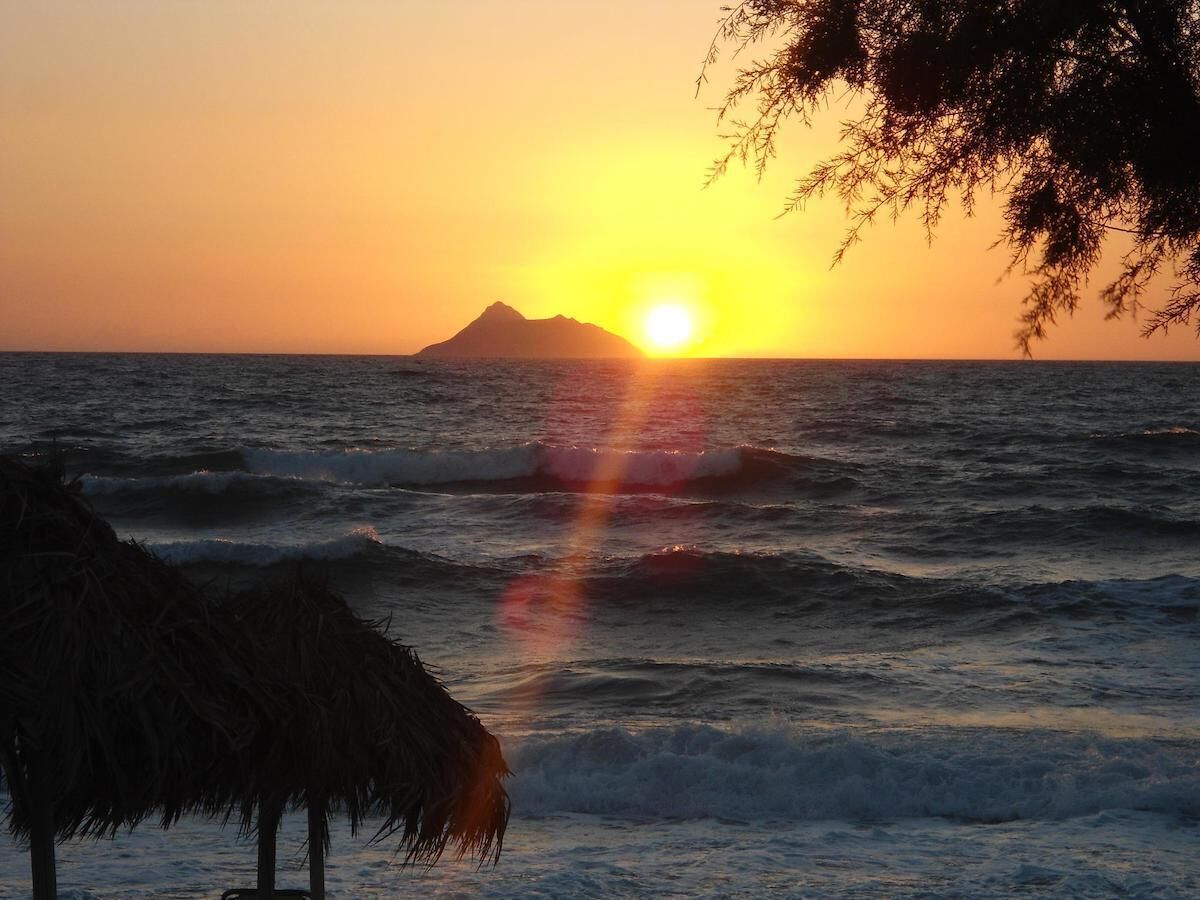 Een zonsondergang boven de oceaan, met golven en een berg in de verte.