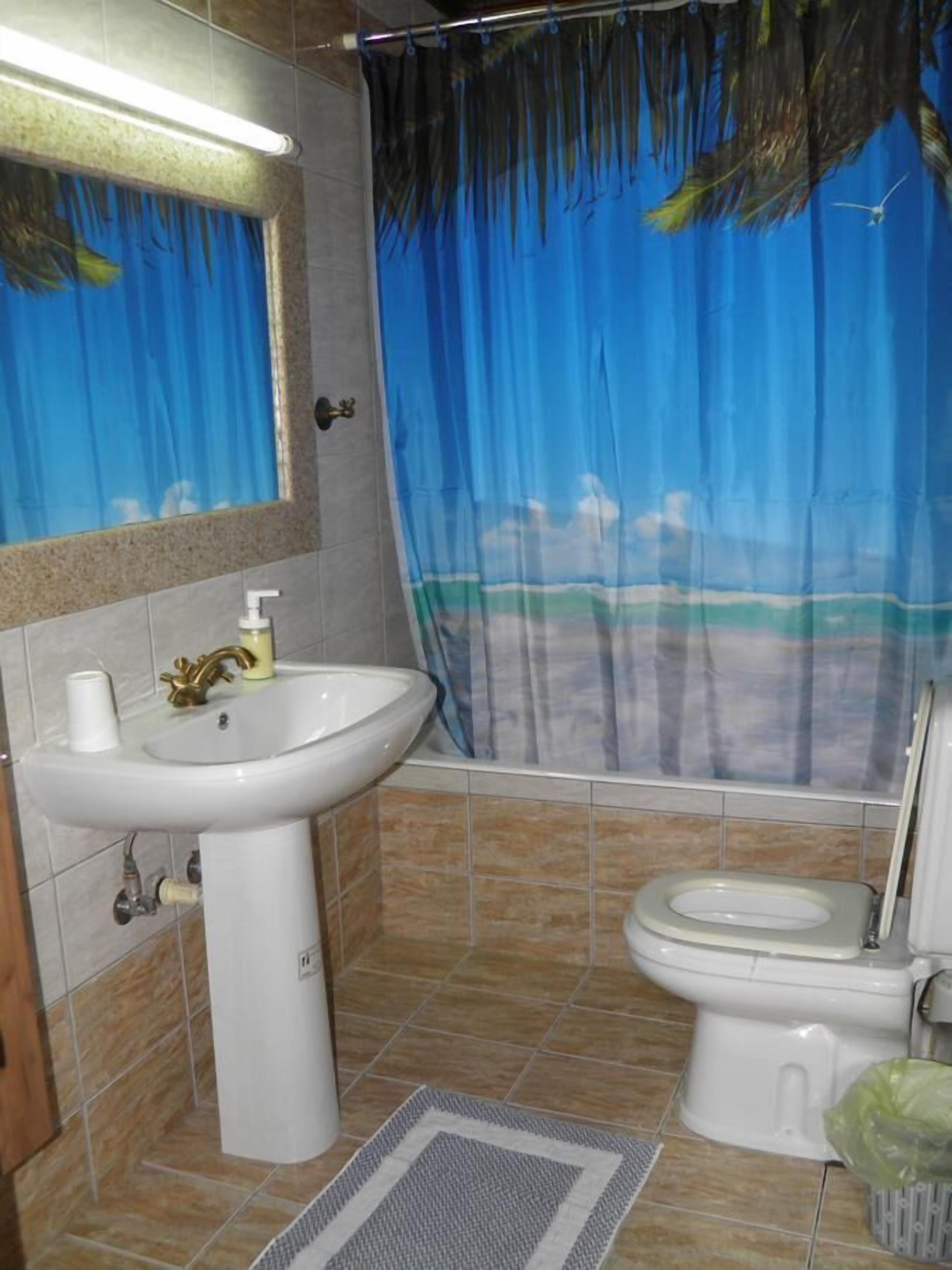 A bathroom with a sink, toilet, and shower curtain depicting a beach scene.