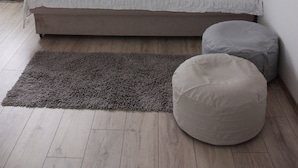 Una habitación minimalista con sofá cama, alfombra gris y un otoman redondo.