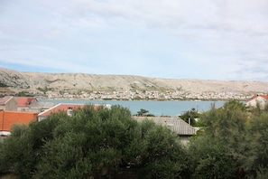 A coastal town with buildings along the shoreline and a mountainous backdrop. - Apartment Sanja (Pag)