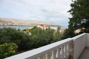 A balcony with a white balustrade overlooking a coastal town with buildings and a body of water. - Apartment Sanja (Pag)