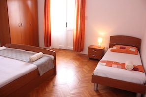 A hotel room with two beds, wooden flooring, a wardrobe, and a nightstand with a lamp. - Apartment Sanja (Pag)