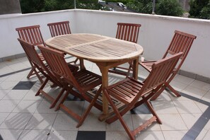 A round wooden table with six chairs on a tiled balcony. - Apartment Sanja (Pag)