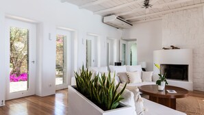 A modern living room with a white sofa, a coffee table, and a fireplace. There are multiple doors leading to outdoor areas. - Infinity View and SUNSET Over Aegean Sea, PRIVCY & Security (Mykonos)