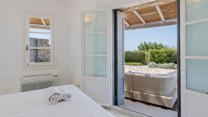A bedroom with a bed, a window, and a view of an outdoor seating area. - Infinity View and SUNSET Over Aegean Sea, PRIVCY & Security (Mykonos)