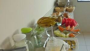 Una mesa de buffet con diversos alimentos y bebidas, entre ellos frutas, pastelería y una jarra de zumo de naranja.