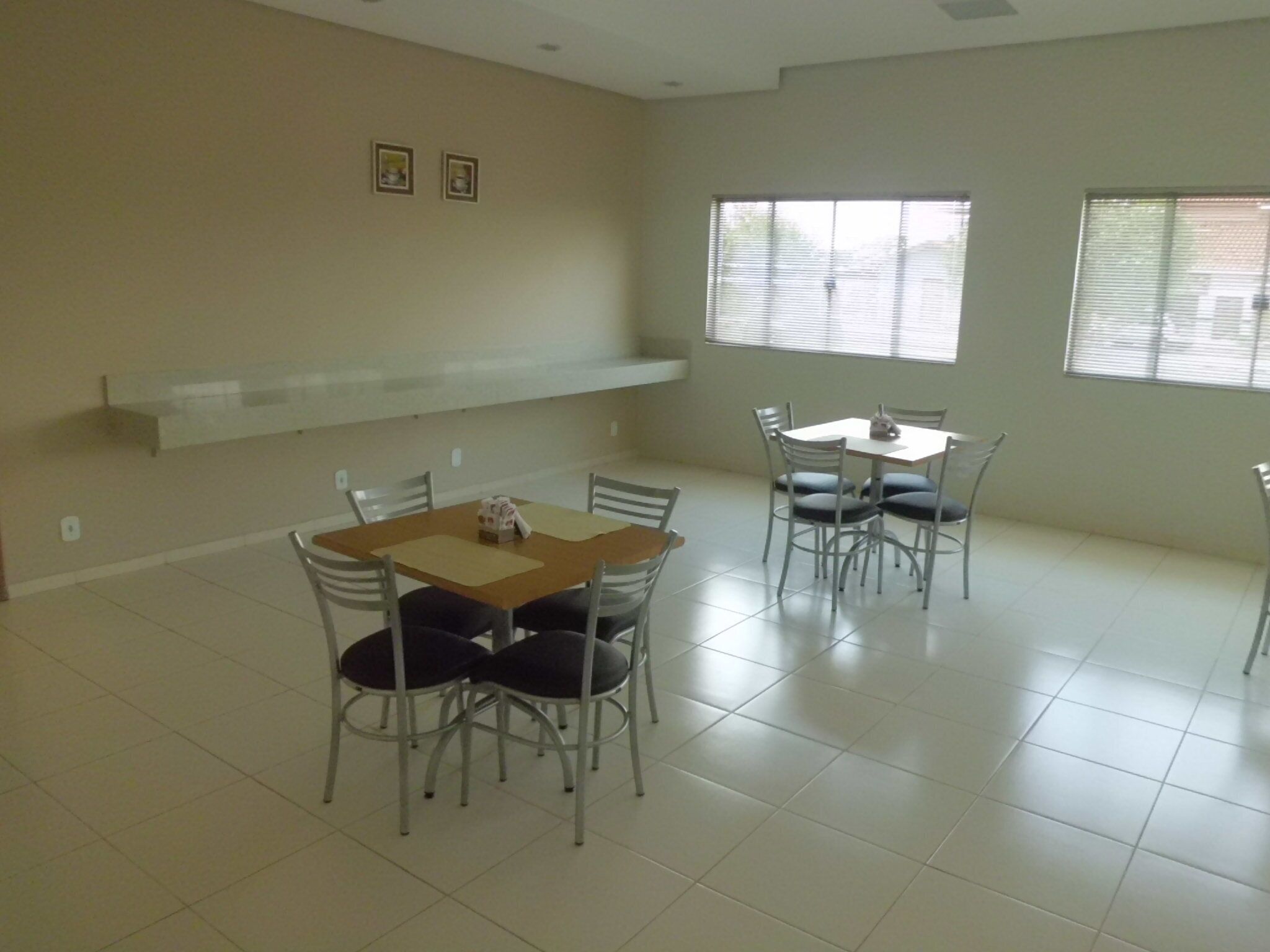 Una habitación amplia con una mesa de comedor y sillas, un estante blanco y ventanas grandes con persianas.