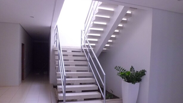Una escalera moderna con barandas de metal y escalones blancos, que conduce a una zona de descanso con una planta en maceta.
