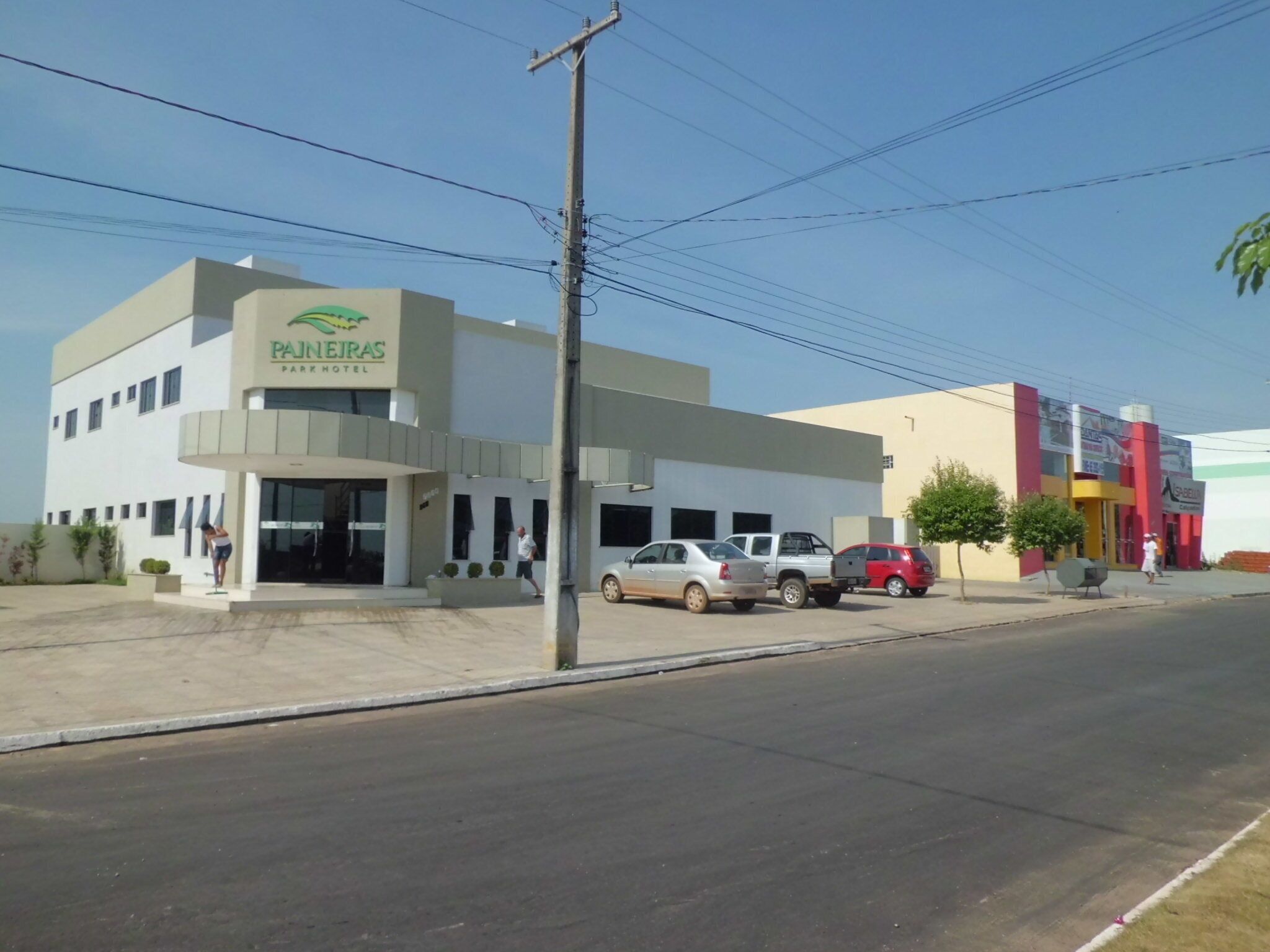 A hotel named 'PAINHEIRAS PARQUE HOTEL' with a modern design, a parking lot, and a street with parked cars.