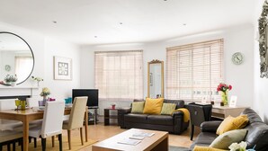 A modern living room with a dining area, a sofa set, a coffee table, and a TV. - 3-bedroom Apartment Lancaster Gate (London)