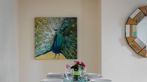 Een eethoek met een tafel voor vier personen, een schilderij van een pauw aan de muur, en een geometrisch spiegelbeeld.