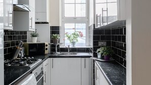 Een kleine keuken met witte kastjes, een zwart aanrecht, een ingebouwde wasmachine en een raam met uitzicht.
