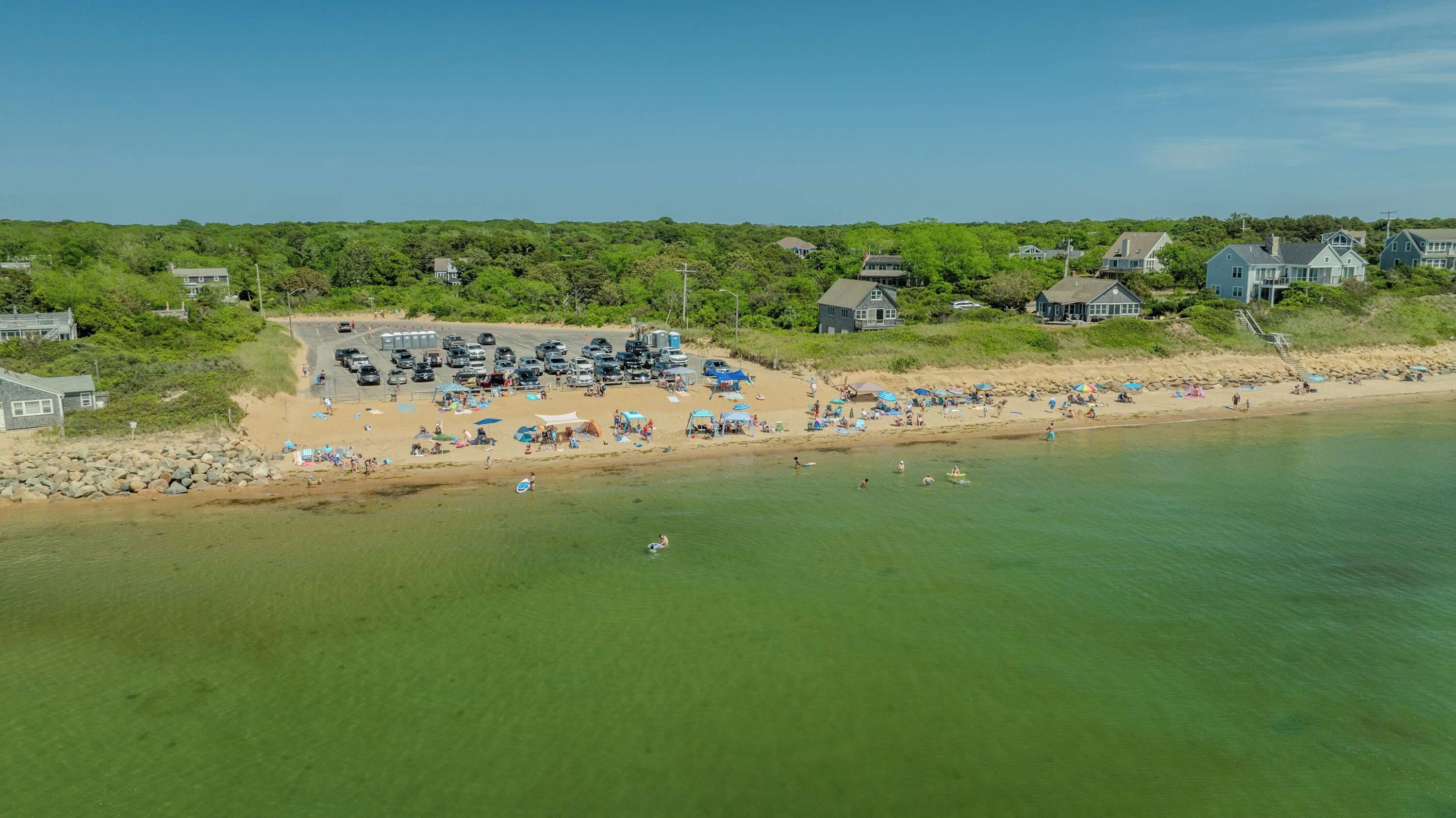 A beachside property with a parking area, beach, and houses in the background.