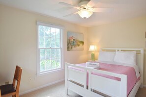 A bedroom with a bed, a chair, a window, a ceiling fan, and a painting on the wall.