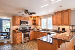A modern kitchen with wooden cabinets, stainless steel appliances, a granite countertop, and a ceiling fan.