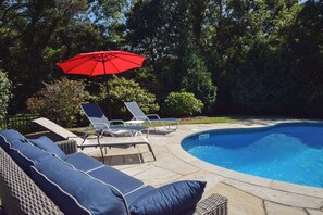 Zona de piscina amb gandules i un parasol vermell.