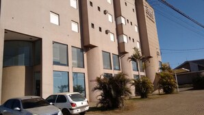 A multi-story hotel building with a beige facade, several windows, and a parking area with two cars. - Hotel Imbau Palace (Imbau)