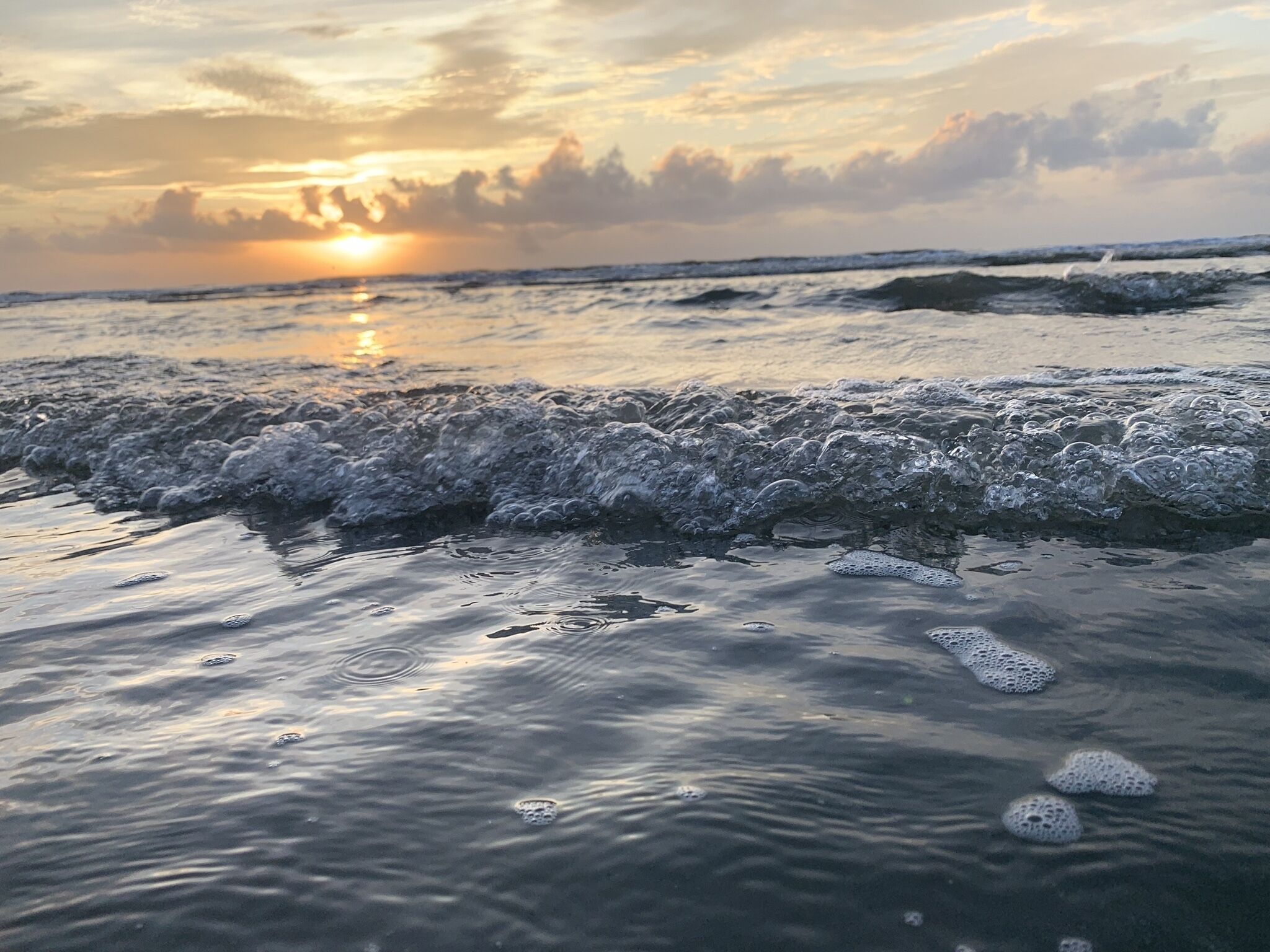 A beach with waves crashing onto the shore and a sunset in the background.
