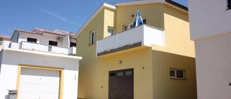 A two-story building with a yellow facade, a white garage door, and a blue awning on the balcony.