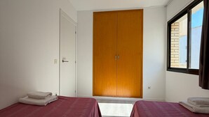 Une chambre avec deux lits, une armoire et une fenêtre.