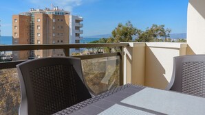 Un balcon avec des fauteuils en osier et une table, d’où l’on peut admirer un immeuble et un ciel dégagé.