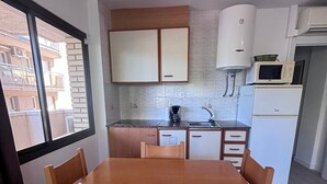 A compact kitchen with a dining table, cabinets, a microwave, and a refrigerator.