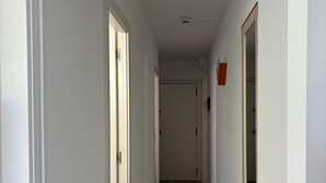 A narrow hallway with white walls and wooden flooring, leading to a door at the end.