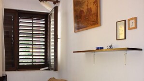 A room with a sofa, a window with blinds, a painting, and a shelf with items.